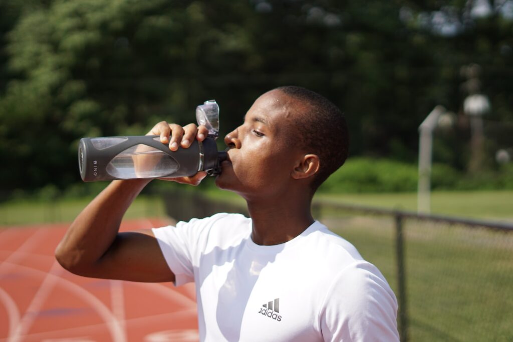 man in white crew neck t-shirt drinking cbd water from black sports bottle
